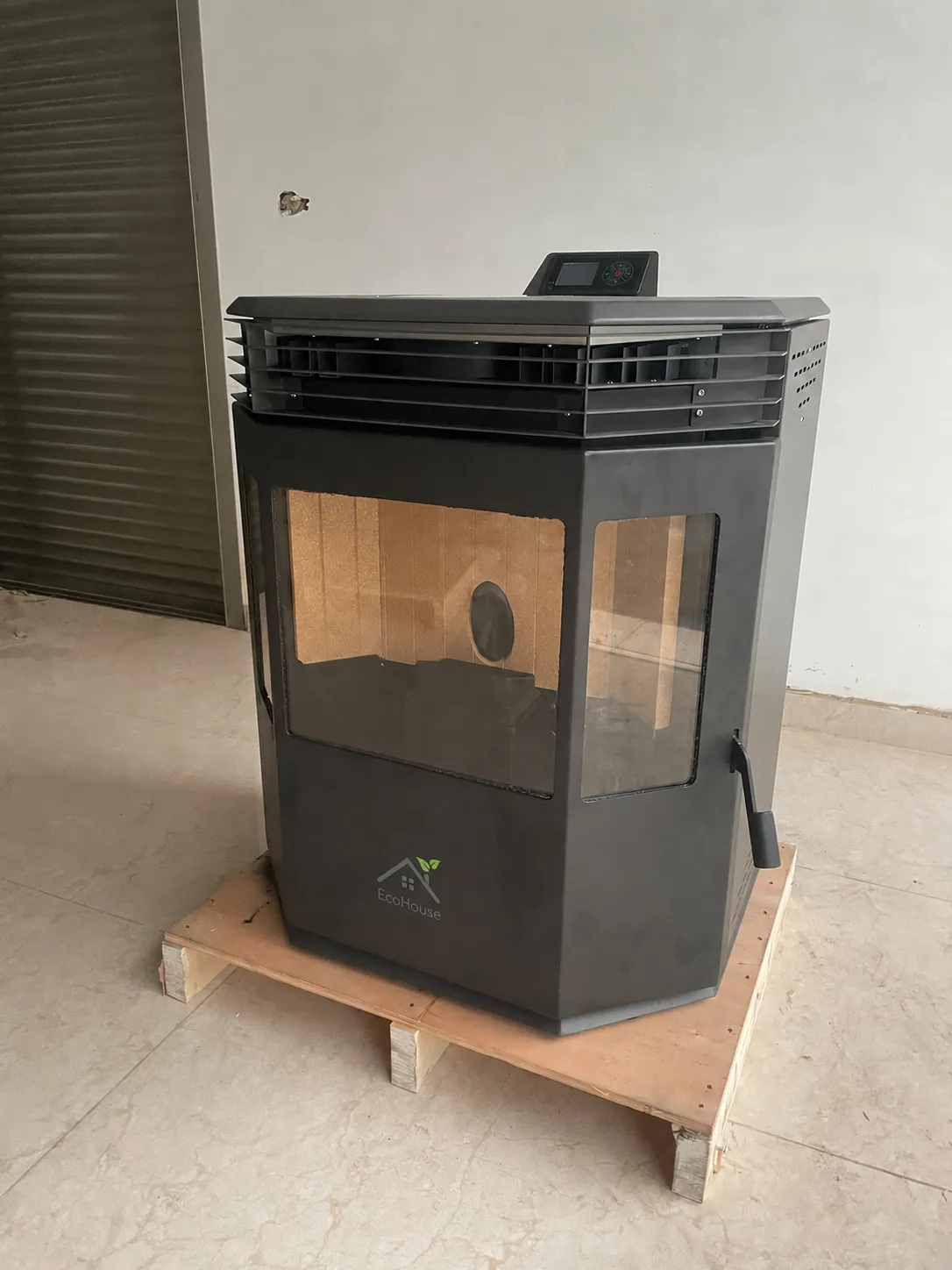 Black faceted pellet stove with a wide panoramic window on a wooden pallet