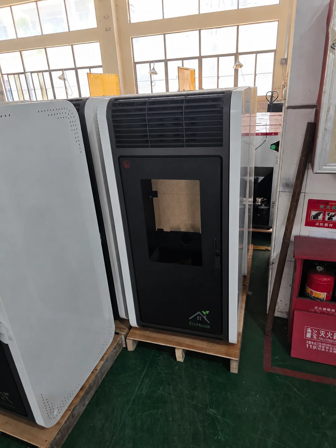 White and black pellet stove on a wooden pallet in a warehouse